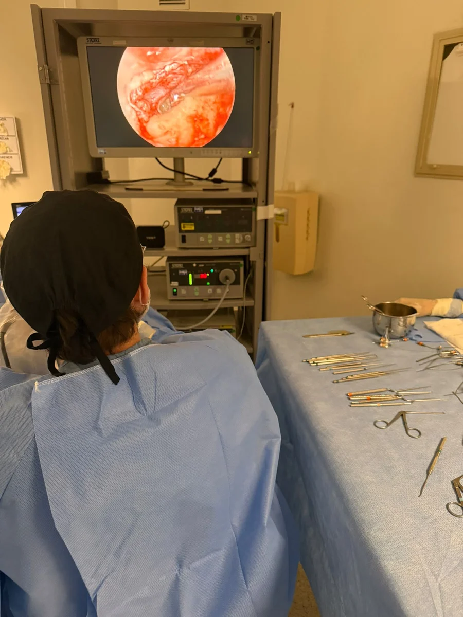 Dr. Caio Alves, de costas e paramentado, observando o monitor durante uma estapedotomia endoscópica