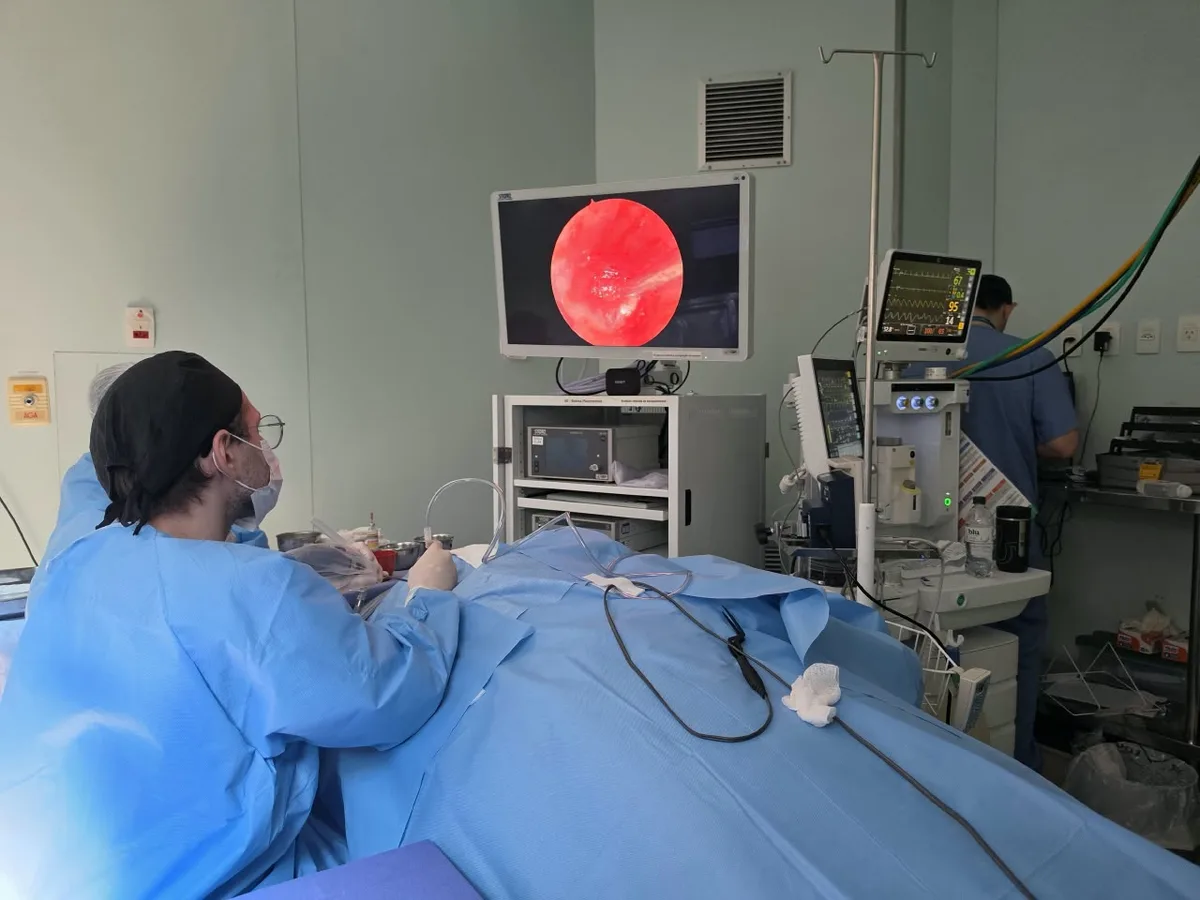 Dr. Caio Alves realizando uma timpanoplastia com endoscópio; a imagem do ouvido aparece no monitor